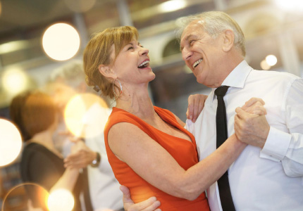 Natural Pharmaceuticals Movisan™ Collagen II Starsza para tańcząca radośnie podczas imprezy towarzyskiej w eleganckim wnętrzu.