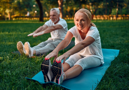 Natural Pharmaceuticals Movisan™ Collagen II Para seniorów ćwicząca rozciąganie na matach do jogi w parku podczas słonecznego dnia.