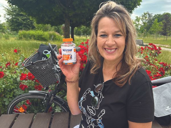 Natural Pharmaceuticals Movisan™ Collagen II Kobieta siedzi na ławce w parku i uśmiechając się, trzyma suplement diety Movisan Collagen II wspierający zdrowie stawów.