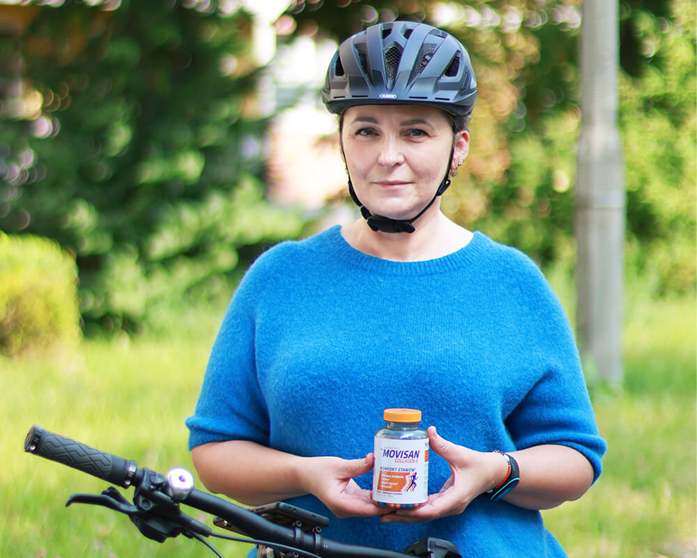 Natural Pharmaceuticals Movisan® Collagen II Kobieta siedząca na rowerze i trzymająca butelkę suplementu diety Movisan® Collagen II na tle zielonych drzew, symbolizująca zdrowie i wsparcie stawów.